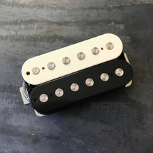 Two Sonic pickups, one cream and one black, stacked on a dark textured surface. The pickups feature silver metal pole pieces and a white brand label.
