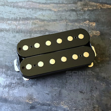 A black guitar humbucker pickup with nickel plated pole pieces, resting on a textured dark gray surface. A faint 'SONIC Pickups' watermark is visible on the right side.