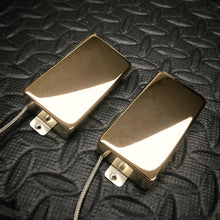 Two shiny metallic guitar pickups with attached wires, photographed on a textured black surface.