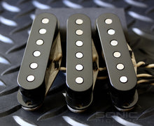 Three black single coil pickups with shiny magnets on a dark background.