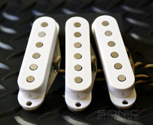 Three white single coil pickups with shiny magnets on a dark background.