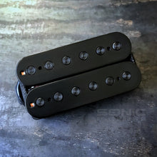 A black humbucker guitar pickup with visible wire windings and magnetic poles.